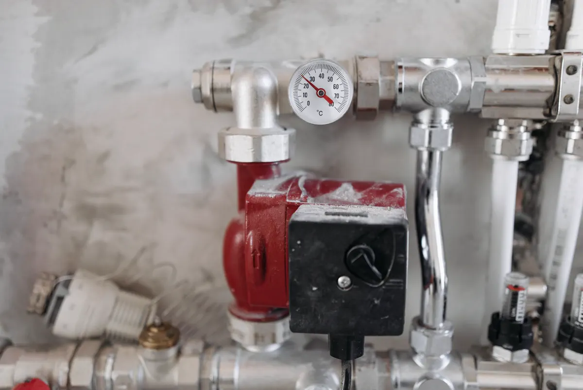 Pressure gauge, pump and valves on the pipework above a domestic boiler