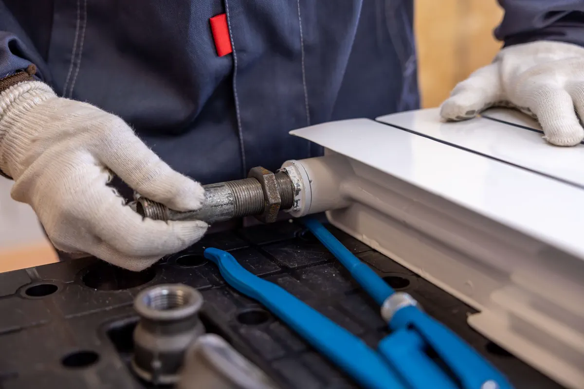 Engineer assembling radiator pipework and valves with hand tools