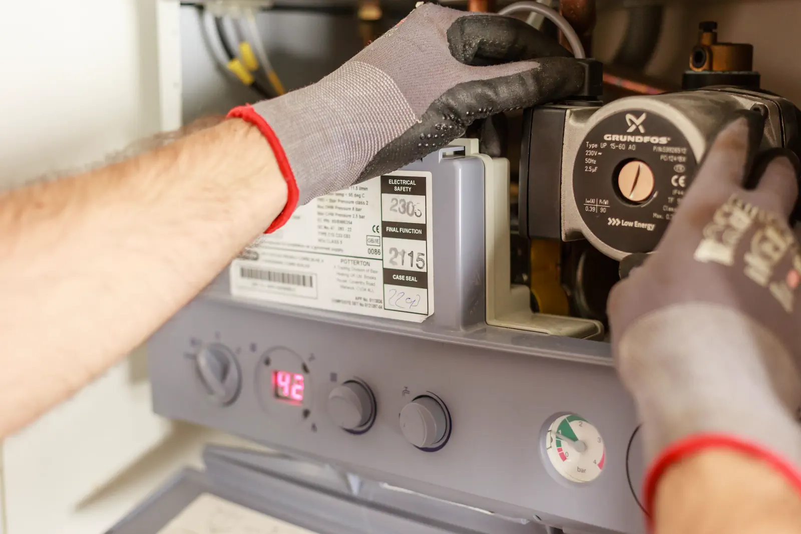 Heating engineer in work gloves servicing the internal components of a wall-mounted gas boiler