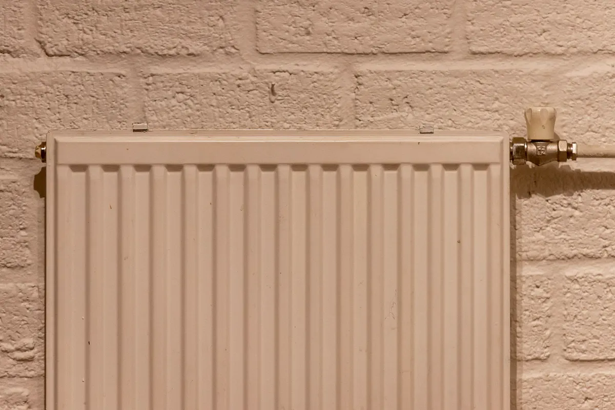 Panel radiator with a valve, mounted on a painted brick wall