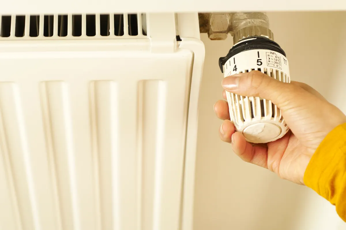 Hand adjusting the thermostatic valve on a panel radiator