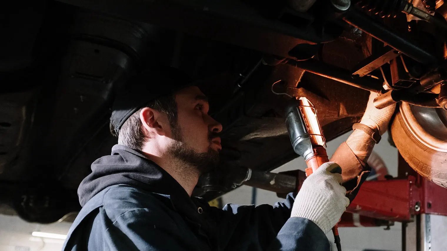 A mechanic working underneath a raised vehicle with an inspection lamp.